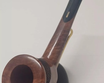 Pode incluir: Um cachimbo de madeira marrom com um bocal preto e uma banda dourada. O cachimbo está em um suporte preto.