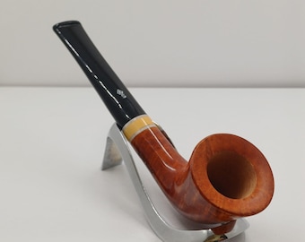 May include: A traditional tobacco pipe with a curved, reddish-brown bowl and a black stem. The pipe has a light-coloured band and is displayed on a silver stand. The pipe is designed for smoking.