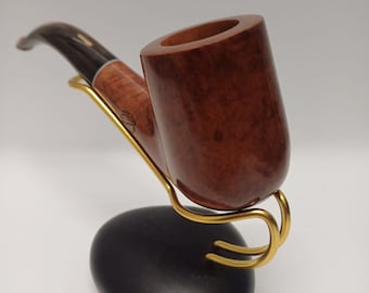 May include: A brown wooden pipe with a black stem and a gold metal stand. The pipe is resting on a black stone base.