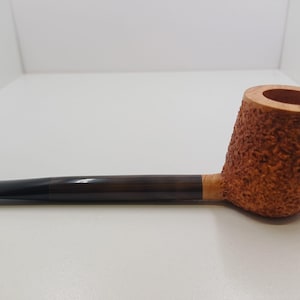 May include: A tobacco pipe with a dark brown stem and a textured, light brown bowl. The bowl has a rounded shape and a smooth, circular opening. The pipe is made of wood and has a classic design.