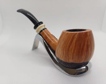May include: A wooden tobacco pipe with a curved, black stem and a light-coloured, rounded bowl. The pipe rests on a silver-coloured metal stand. The bowl has a dark brown base and a lighter, wood-grain pattern.