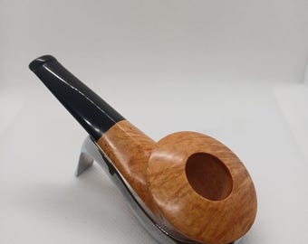 May include: A wooden tobacco pipe with a black stem and a light brown bowl. The pipe rests on a silver-coloured metal stand. The bowl has a large opening. The pipe is designed for smoking tobacco.