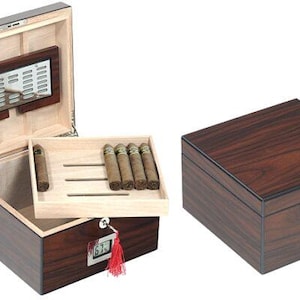 May include: A dark brown wooden humidor, with a tray of cigars visible inside when open. The interior is light-coloured wood. A digital display is on the front. A closed humidor is also shown.