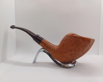 May include: A light brown tobacco pipe with a curved stem and a dark brown mouthpiece. The pipe rests on a silver-colored stand, showcasing its natural wood grain and smooth finish. The pipe is a classic smoking accessory.