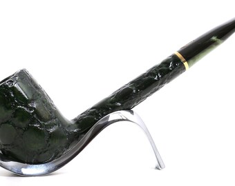 May include: A dark green tobacco pipe with a textured, bumpy surface and a smooth, tapered stem. The pipe features a thin gold-coloured band where the bowl meets the stem and is supported by a curved, polished silver-toned metal stand.