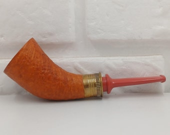 May include: A curved tobacco pipe with a reddish-orange bowl and a red stem. The bowl is made of a textured, light-colored wood, and the stem is connected to the bowl with a brass band.
