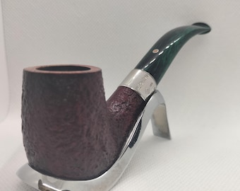 May include: A tobacco pipe with a dark brown bowl and a green stem. The pipe is resting on a silver-colored stand. The bowl has a textured surface, and the stem has a silver band near the connection to the bowl.