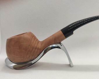 May include: A wooden tobacco pipe with a curved, black stem. The pipe is light brown and rests on a silver-colored stand. The pipe has a rounded bowl and a smooth finish, suggesting it is made of high-quality wood.