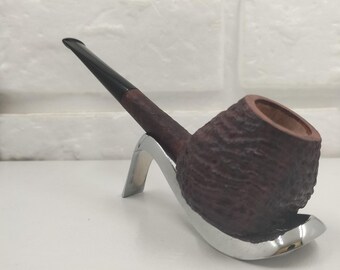 May include: A tobacco pipe with a dark brown, textured bowl and a smooth black stem, resting on a polished silver-colored metal stand. The pipe features a deep, rustic finish on the bowl and a tapered mouthpiece, presented on a curved base.