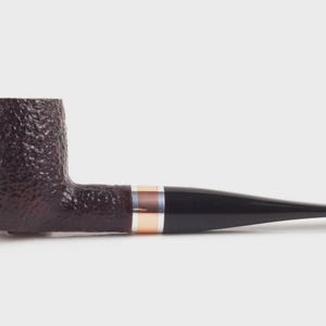 May include: A traditional tobacco pipe with a dark brown, textured bowl and a black stem. The pipe has a decorative band with gold and silver accents. The pipe is designed for smoking tobacco.
