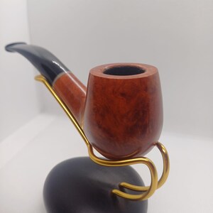 May include: A wooden pipe with a brown bowl and a black stem, resting on a gold metal stand with a black base.