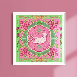 Könnte beinhalten: Eine weiße Katze mit rosa und grünen floralen Details in einem quadratischen Rahmen. Die Katze liegt auf dem Rücken mit den Pfoten in der Luft. Der Hintergrund ist hellrosa.