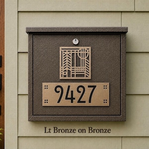 May include: A square bronze-colored metal mailbox featuring a textured finish, a central key lock, and a decorative geometric cutout design. Below the cutout, a rectangular plaque displays the house number 9427 in black digits.