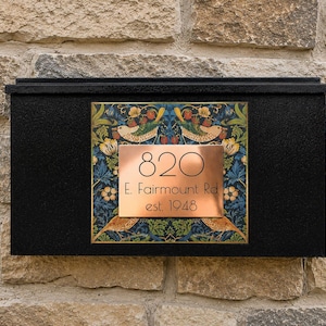 May include: A black rectangular mailbox featuring a central copper plaque with the text 820 E. Fairmount Rd est. 1948. The plaque is set against a square panel decorated with a colorful botanical pattern of birds, strawberries, and green foliage.