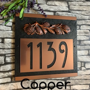 May include: Copper house number sign with black background and pine cone design. The number 1139 is displayed in a large font. The word "Copper" is written below the number.