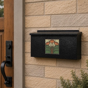 May include: A black metal wall-mounted mailbox featuring a textured finish and a central square decorative tile. The tile displays a stylized floral pattern in shades of orange, green, and cream, set against a light-colored brick wall exterior.