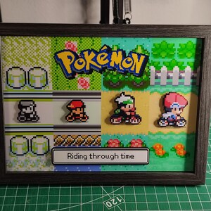 May include: Framed pixel art featuring the Pokémon logo and characters. The artwork includes a variety of colorful backgrounds and characters, with the text "Riding through time" at the bottom. The frame is dark gray.