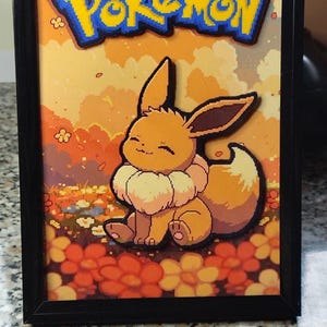 Può includere: Un'opera d'arte incorniciata a strati 3D che raffigura il Pokémon Eevee seduto in un campo di fiori arancioni e gialli. La parola Pokémon è visualizzata in testo blu e giallo in alto. Lo sfondo mostra un cielo al tramonto con nuvole.
