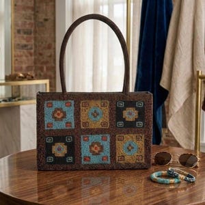 Peut inclure: Un sac à main rectangulaire recouvert de petites perles présentant une grille de six carrés dans des tons de bleu, d'or et de noir avec des motifs géométriques. Le sac possède une anse arrondie et est accompagné de lunettes de soleil rondes.
