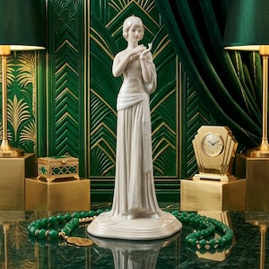 May include: A white porcelain figurine of a standing person wearing a long, flowing gown with a draped sash. The figure has short hair and is posed with hands near the chest. The smooth, glossy surface reflects light, highlighting the sculpted folds of the fabric.
