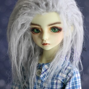 May include: A doll with long, white, fluffy hair wearing a blue and white plaid shirt. The doll has green eyes and a light complexion.