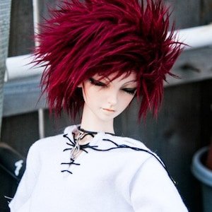 May include: A doll with bright red spiky hair wearing a white shirt with black stitching and a black choker.