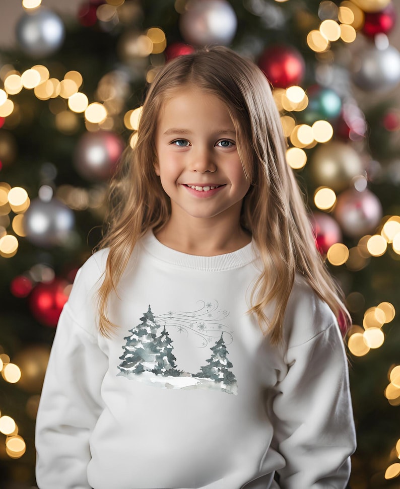 May include: White sweatshirt for kids features a watercolor-style winter scene with two evergreen trees and snowflakes. The design is subtle and charming, perfect for the holiday season.  The sweatshirt is soft and comfortable, ideal for everyday wear or special occasions.  A great gift for children who love winter and nature.