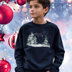 May include: A navy blue sweatshirt with a winter landscape design. The graphic shows snow-covered trees and snowflakes in grey and white. The sweatshirt has a crew neck.