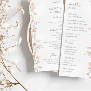 Könnte beinhalten: Hochzeitszeremonie-Programm mit floralem Rand. Das Programm enthält die Namen der Hochzeitsgesellschaft, des Standesbeamten und die Reihenfolge der Zeremonie. Der Text lautet "Willkommen zur Hochzeit von Hannah & Theo, 6. Juli 2023".