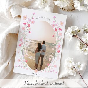 Op de afbeelding: Een huwelijksuitnodiging met een bloemige rand en een foto van een stel op een strand. De tekst op de uitnodiging luidt "Harper & Lucas" en "08.23.25".