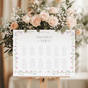 Puede incluir: Un plano de asientos de boda con un borde floral. El plano está titulado "Amanda y Theo" y enumera los nombres de los invitados por número de mesa. El borde floral presenta flores rosas, moradas y azules.