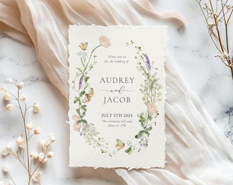 May include: A wedding invitation with a floral wreath design. The invitation features the names "Audrey and Jacob" and the date "July 5th 2025". The invitation is on textured paper with a soft, neutral background.