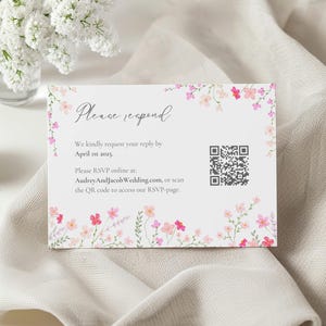 May include: A white RSVP card with a pink floral border. The text reads "Please respond" and includes a QR code. The text also states "We kindly request your reply by 1st April 2025. Please RSVP online at: AudreyAndJacobWedding.com, or scan the QR code to access our RSVP page."