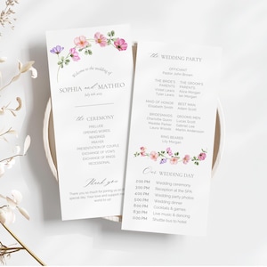 Könnte beinhalten: Zwei weiße Hochzeitskarten mit floralen Verzierungen. Die Karten enthalten die Namen des Paares, Zeremoniedetails, Hochzeitsgesellschaft und Zeitplan. Sie sind mit Aquarellblumen in Rosa, Lila und Grün verziert.