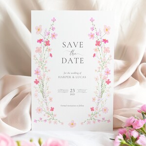 Op de afbeelding: Save the date-kaart met een roze bloemenrand. De kaart staat "Save the Date" voor de bruiloft van Harper & Lucas, zaterdag 23 augustus 2025. Formele uitnodiging volgt.