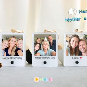 May include: Three white photo frames with family photos, each with a gold-colored keychain attachment. The frames have the text "Happy Mother's Day" and "I like us" printed on them. A pinecone and a wooden figurine are in the background.