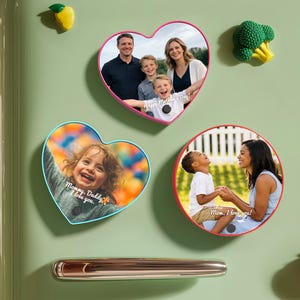 Könnte beinhalten: Eine Sammlung von Familienfoto-Magneten in Herz- und Kreisform, die an einem grünen Kühlschrank befestigt sind. Die Magnete zeigen Familienfotos und die Sätze "Mommy, Daddy I love you!" und "Mom, I love you!" Dekorative Obstmagnete sind ebenfalls vorhanden.