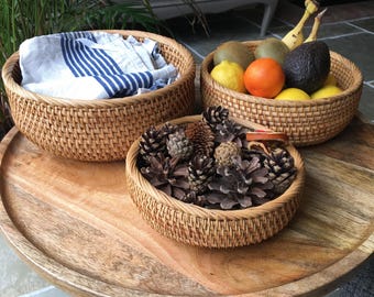 May include: Three woven wicker baskets on a wooden table. The baskets are filled with various items, including a blue and white striped towel, fruit, and pine cones.