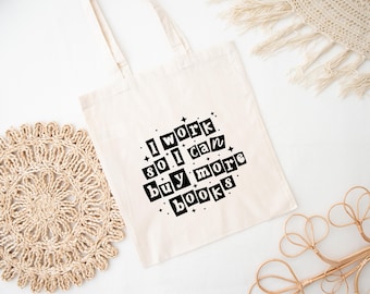 May include: A white tote bag with black text that reads "I work so I can buy more books". The text is in a bold, blocky font and is surrounded by small stars.