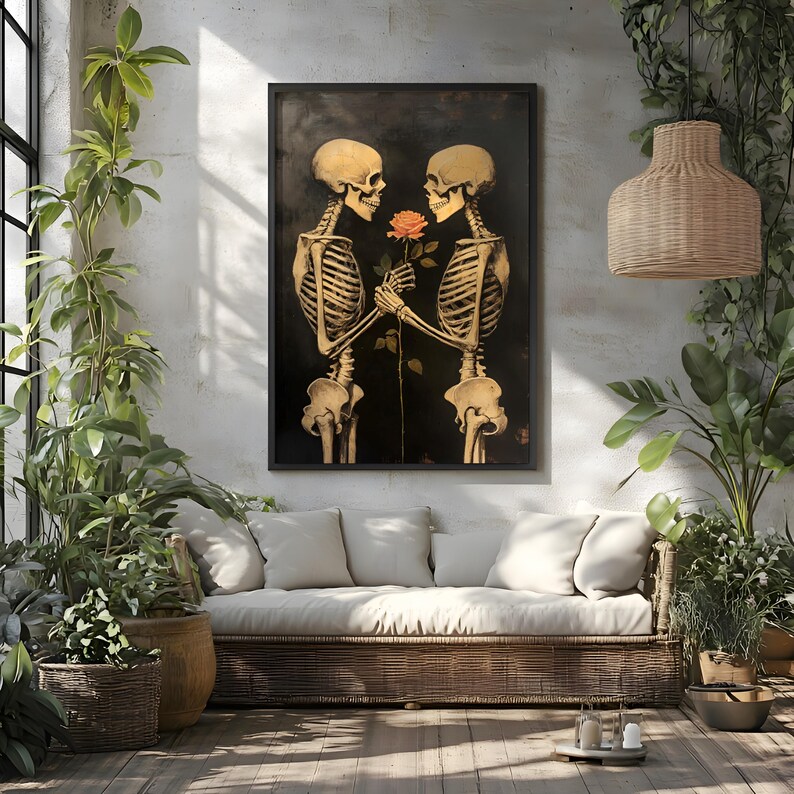 May include: Framed artwork showing two skeletons in a romantic pose, holding a rose. The skeletons are golden against a dark backdrop. The print hangs above a wicker sofa, surrounded by plants, creating a gothic yet cozy atmosphere.
