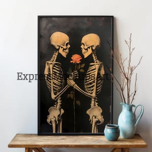May include: A framed art print depicting two skeletons sharing a rose against a dark backdrop. The skeletons are in a loving embrace, with the text "Express Mindful Art" visible. The artwork is displayed on a wooden table, with a vase and pot.