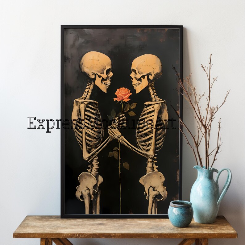 May include: A framed art print depicting two skeletons sharing a rose against a dark backdrop. The skeletons are in a loving embrace, with the text "Express Mindful Art" visible. The artwork is displayed on a wooden table, with a vase and pot.