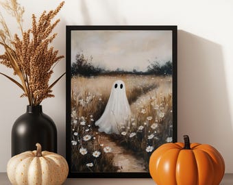 May include: A framed art print depicts a white ghost in a field of wildflowers. A black vase with dried wheat and two pumpkins, one cream-colored and one orange, are in front of the artwork. The artwork has a black frame.