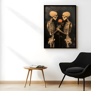 May include: A framed print depicting two skeletons, rendered in sepia tones, holding a rose against a dark backdrop. The artwork is mounted on a white wall, with a black chair and a wooden side table visible in the foreground. The overall aesthetic is gothic.