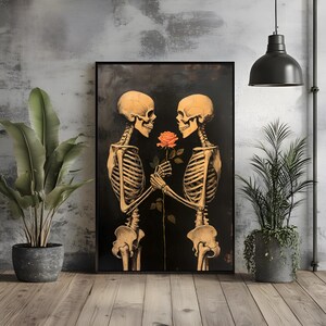 May include: Framed art print showing two skeletons, rendered in a warm golden tone, sharing a rose against a dark backdrop. The rose is a vibrant orange. The artwork is displayed in a room with plants and a dark pendant light.