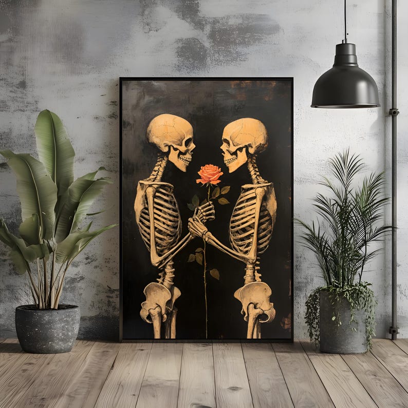 May include: Framed art print showing two skeletons, rendered in a warm golden tone, sharing a rose against a dark backdrop. The rose is a vibrant orange. The artwork is displayed in a room with plants and a dark pendant light.
