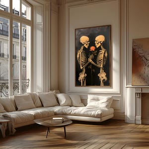 May include: A framed artwork showing two skeletons holding a rose against a dark backdrop. The skeletons are in a loving embrace, with their bony hands gently touching the flower. The artwork is displayed in a well-lit room with a large window and a white sofa.