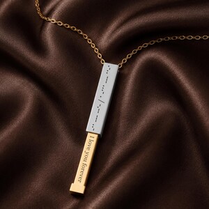 May include: A gold-tone chain necklace featuring a rectangular pendant with a silver-tone outer sleeve engraved with Morse code dots and dashes. The inner gold-tone bar slides out to reveal the engraved text I love you forever in a serif font.