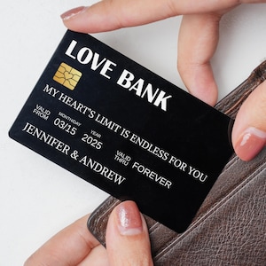 May include: A black card with the words "LOVE BANK" and "MY HEART'S LIMIT IS ENDLESS FOR YOU" in white. The card has a gold heart-shaped design and the names "JENNIFER & ANDREW". The card is dated 03/15/2025 and "VALID THRU FOREVER".