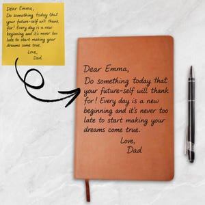 May include: A brown leather-bound notebook with a ribbon bookmark and a black pen. The notebook has the text "Dear Emma, Do something today that your future-self will thank for! Every day is a new beginning and it's never too late to start making your dreams come true. Love, Dad."